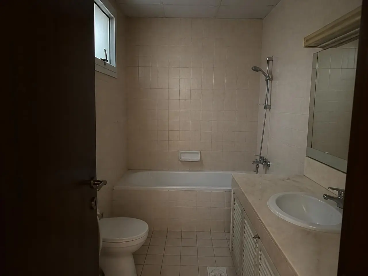 Old bathroom with bathtub and beige tiles before remodeling in JVT Dubai