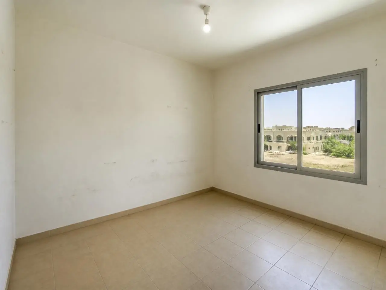 Kids bedroom with scuffed walls and bare bulb before renovation in Motor City Dubai